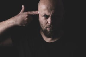 benefits of NLP; a shot of a man pointing a finger towards his head, standing against a dark background