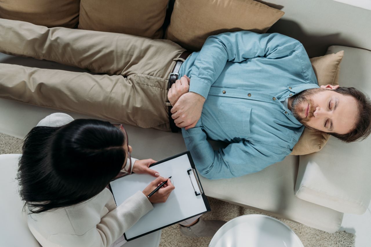 emotional and spiritual healing, a therapist taking notes about a man lying on a sofa 